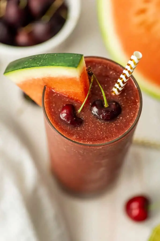 Cherry watermelon smoothie with a watermelon wedge and fresh cherries on top.