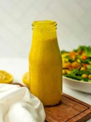 Ginger turmeric dressing sitting on a trivet next to a salad.