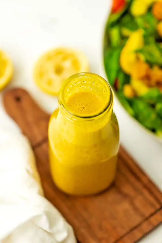 Ginger turmeric dressing in a salad dressing bottle next to a salad.