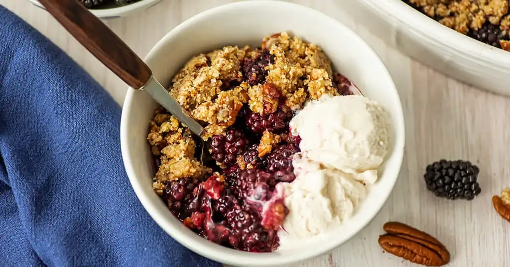 Gluten free blackberry crumble being served in a bowl with vanilla ice cream.
