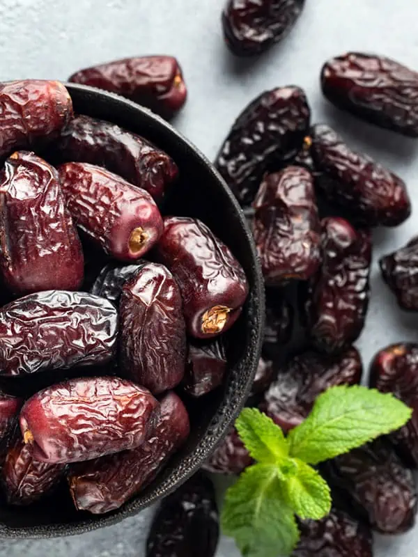 A bowl of medjool dates on a gray surface.