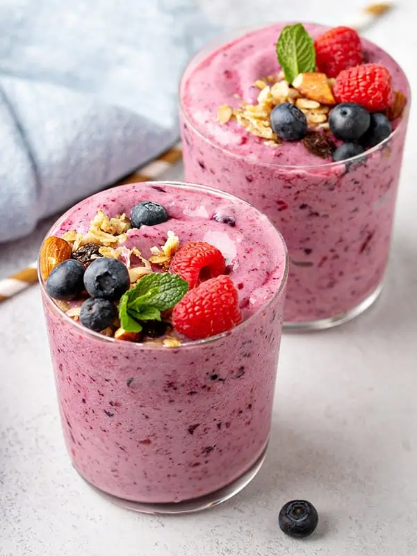 A smoothie sitting on a cutting board with berries laying around it.