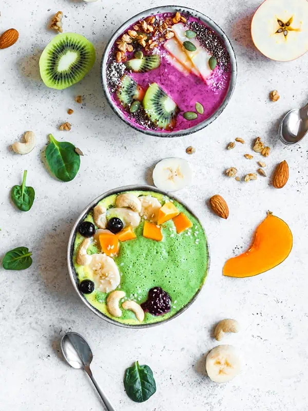 Two smoothie bowls sitting on a white table with a variety of high fiber toppings.