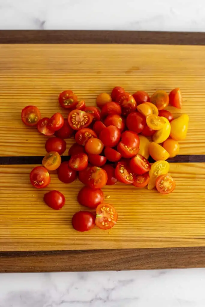 Cherry tomatoes cut in half on a wooden cutting board.
