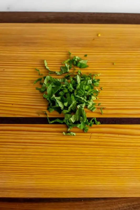 Basil finely chopped on a wooden cutting board.