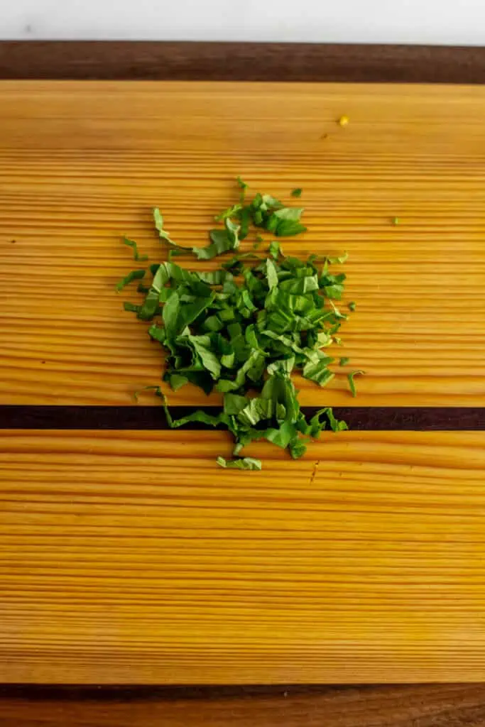 Basil finely chopped on a wooden cutting board. 