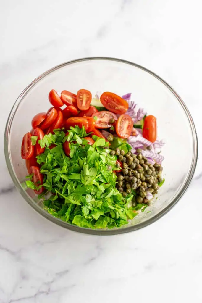 Mediterranean black bean salad with dressing, cucumbers, tomatoes, red onions and parsley in a large bowl.