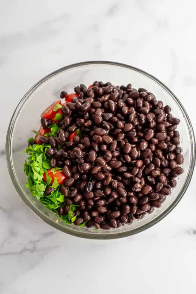 Black beans added to the top of the Mediterranean black bean salad in a large bowl.