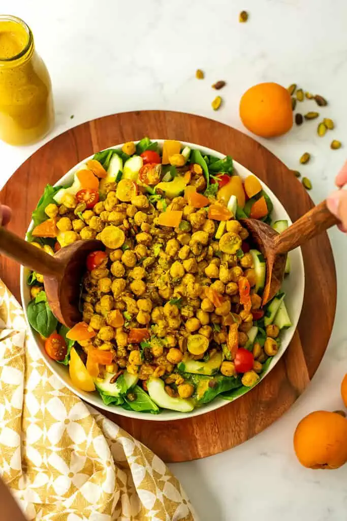 Moroccan chickpea salad in a white bowl on a wooden serving tray with wooden serving spoons.