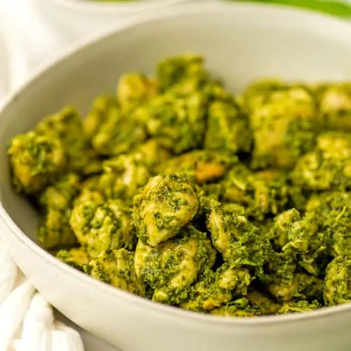 Pesto chicken skillet in a white bowl with a small bowl of pesto in the background.