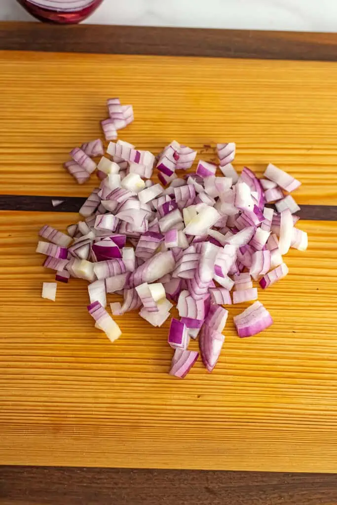 Red onions finely chopped on a wooden cutting board.
