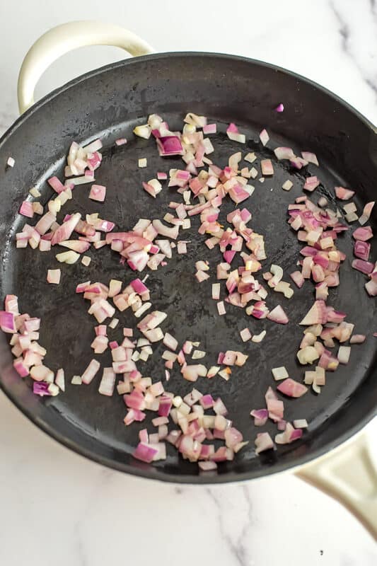 Finely chopped red onions cooking in a cast iron pan.