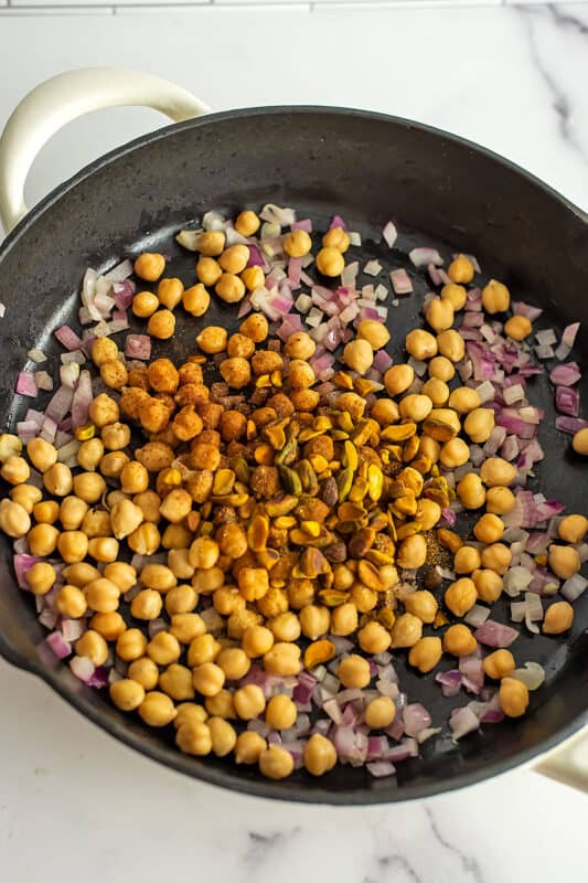 Chickpeas, onions and spices in a large cast iron pan cooking.