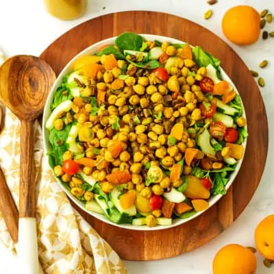 Spinach chickpea salad on a wooden serving place with a wooden spoon next to it.