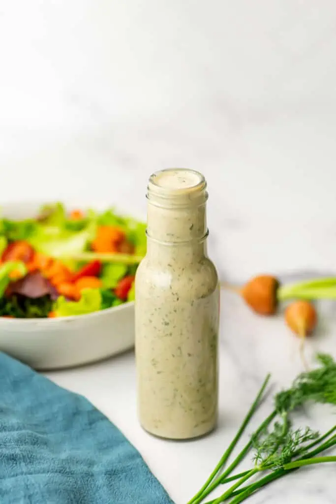 Tahini ranch dressing in a dressing pour bottle with a salad in the background.