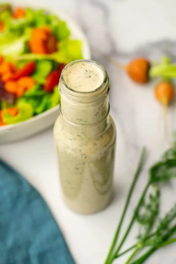 Tahini ranch dressing in a large bottle next to a salad.