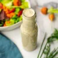 Tahini ranch dressing next to a salad on a white table.