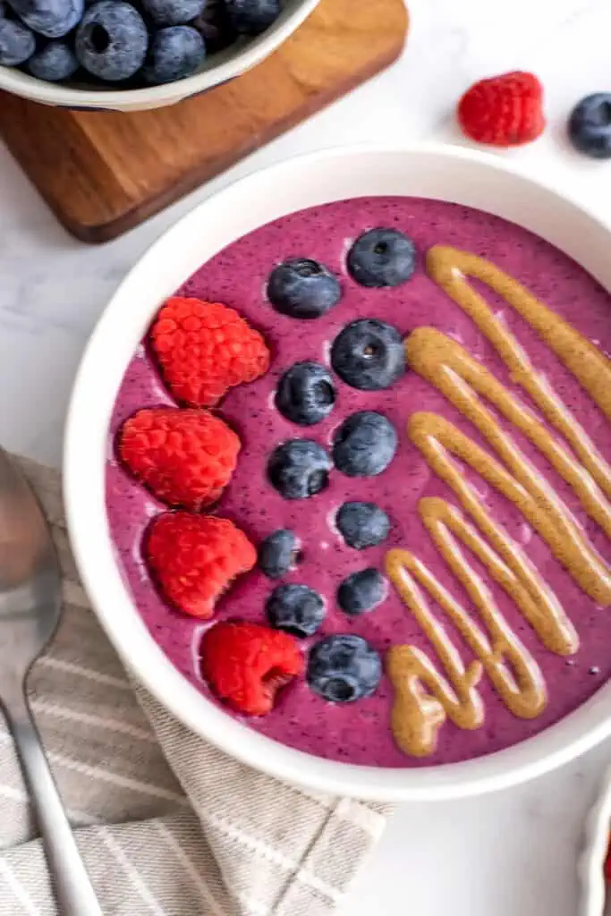 A raspberry blueberry smoothie bowl with almond butter drizzle, blueberries and raspberries for toppings.