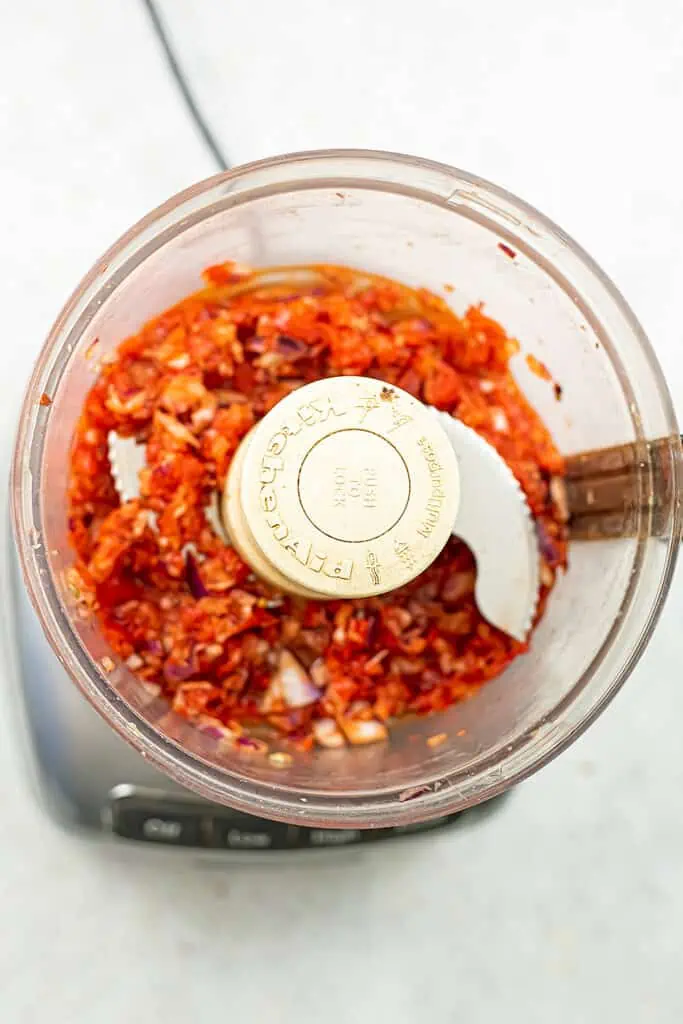 Food processor filled with chopped red pepper and red onion.