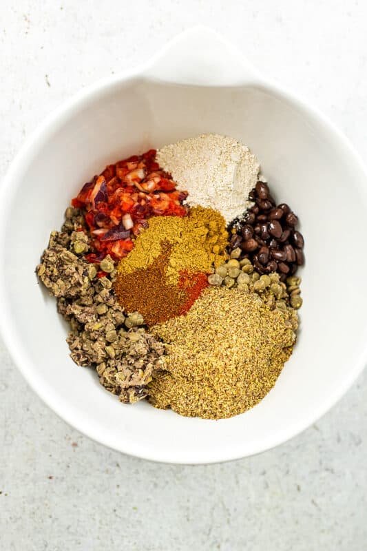 Spices, lentils, black beans and ground flax in large white bowl.