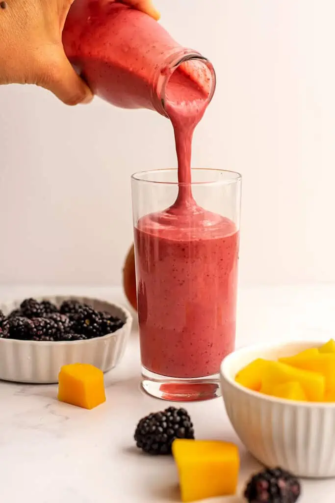 Mango blackberry smoothie being poured into a tall glass.