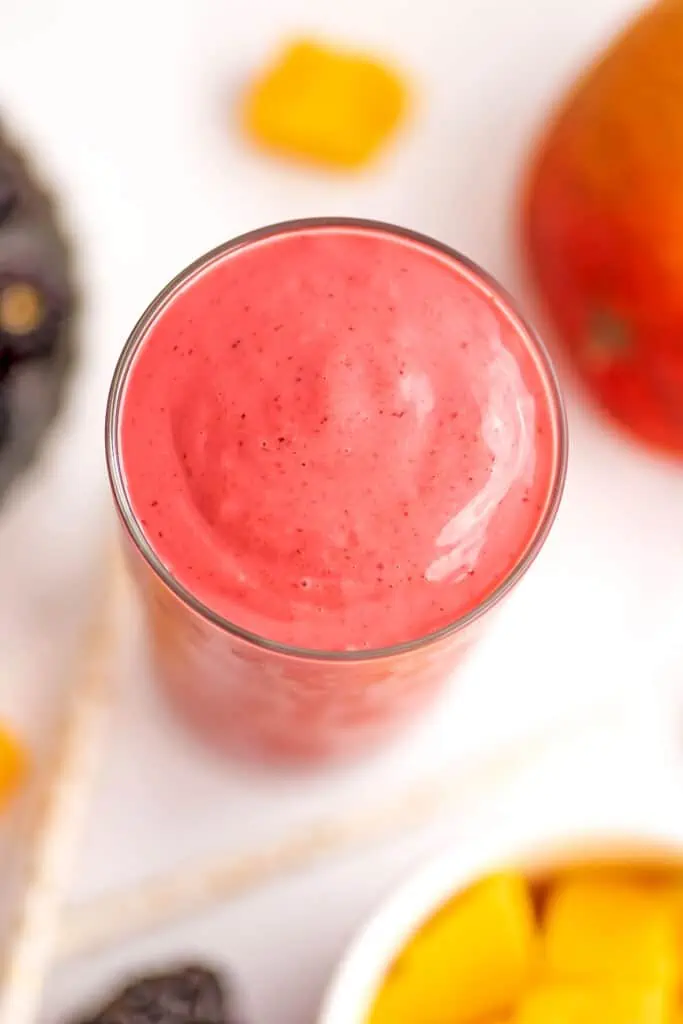 An overhead shot of a blackberry mango smoothie sitting on a white table.