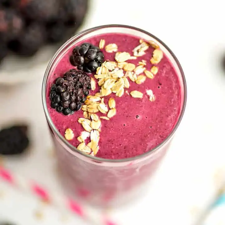 Blackberry oatmeal smoothie in a tall glass with granola and blackberries on top.