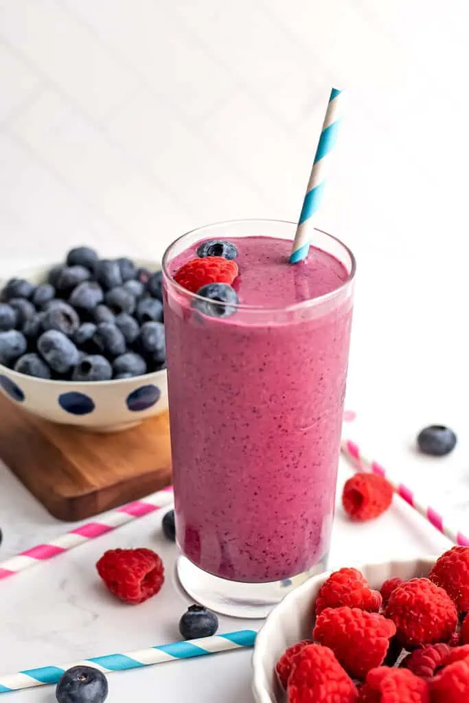 A raspberry blueberry smoothie with blueberries and raspberries on top and a straw.