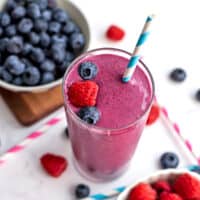 Raspberry blueberry smoothie with a straw and whole raspberries and blueberries on top.