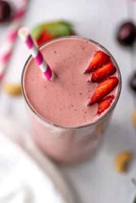 An overhead view of a strawberry cherry smoothie with sliced strawberries and a straw on top.