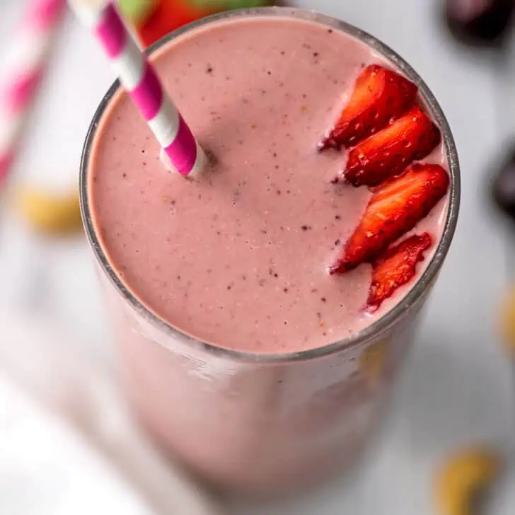 An overhead view of a strawberry cherry smoothie with sliced strawberries and a straw on top.