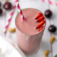 Cherry strawberry smoothie with sliced strawberries on top and a straw.