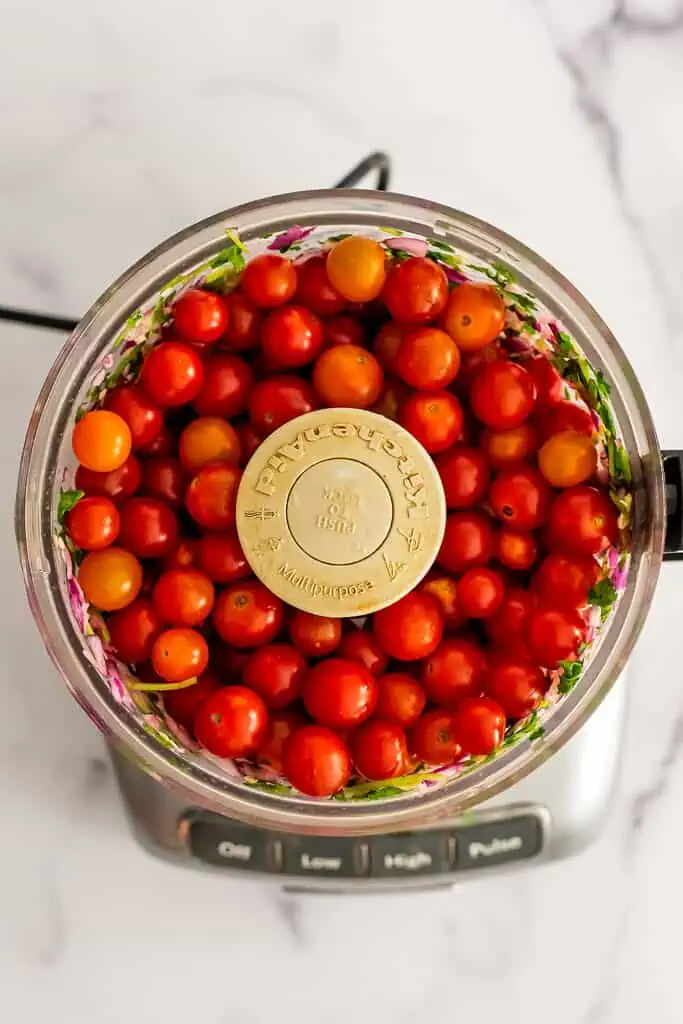 Cherry tomatoes in a food processor with other salsa ingredients.