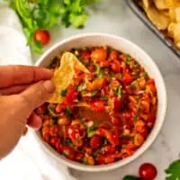 Cherry tomato salsa with a chip being dipped into the salsa.