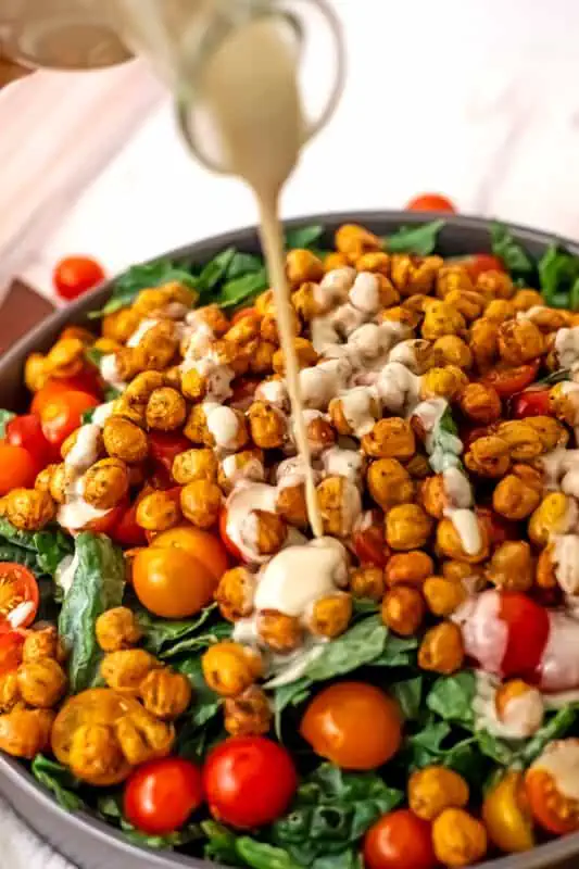 Chickpea kale salad with tahini dressing being poured on it.