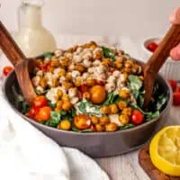 Chickpea kale salad in a gray bowl with wooden salad serving utensils.