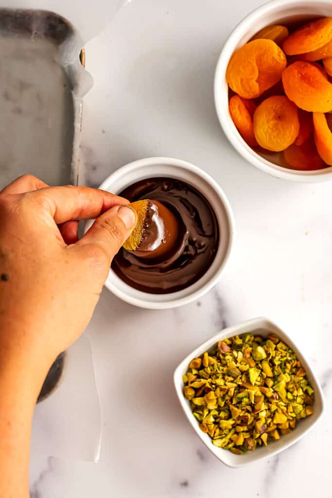 A dried apricot being dipped in melted dark chocolate.