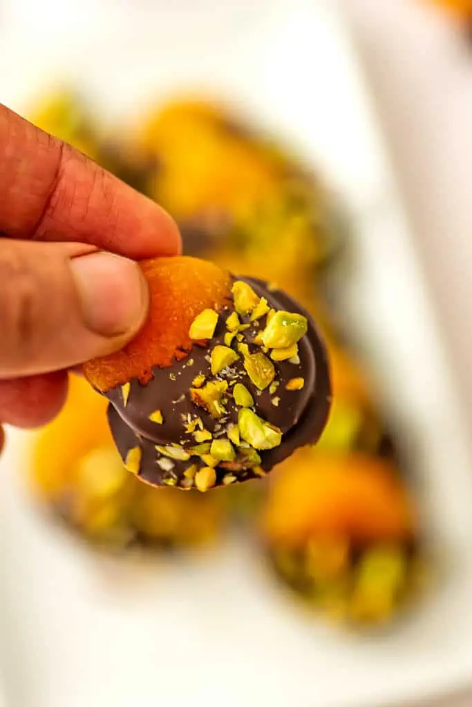 Dark chocolate covered apricot being held.
