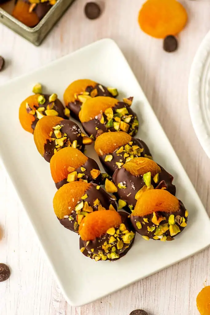 Chocolate dipped apricots lined up for display on a white dish.