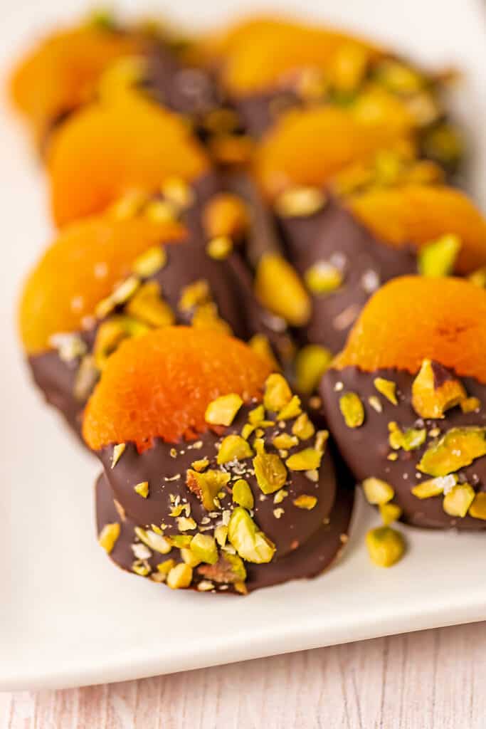 Chocolate covered apricots on a white serving dish.
