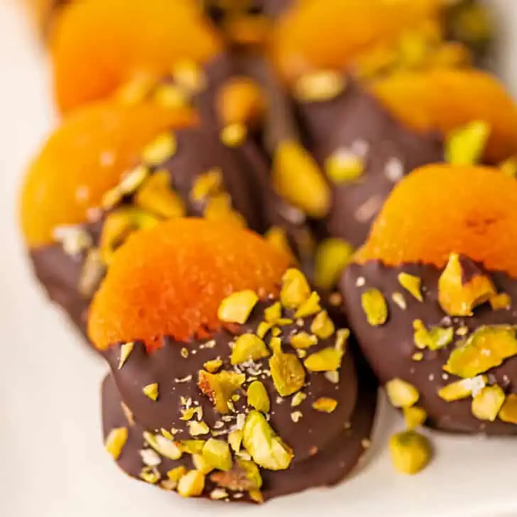 Chocolate covered apricots on a white serving dish.