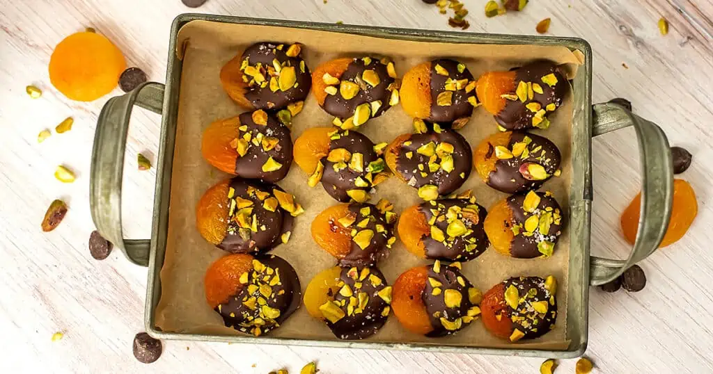 Chocolate covered apricots on a metal serving tray.
