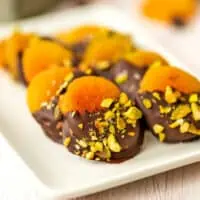 Chocolate dipped apricots with pistachios on a white plate.