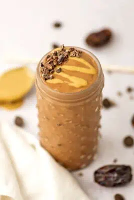Chocolate tahini smoothie in a tall glass with cacao nibs on top.