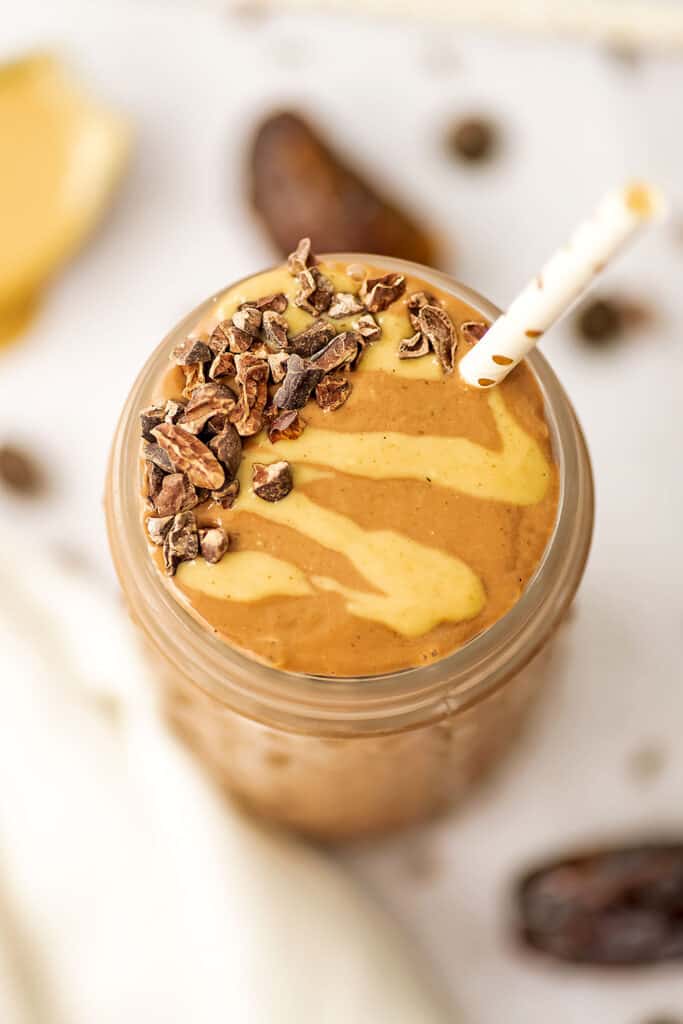 Overhead view of a Chocolate Tahini Smoothie in a glass with cacao nibs and tahini drizzle and a straw. 