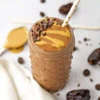 Chocolate tahini smoothie with cacao nibs and a straw.
