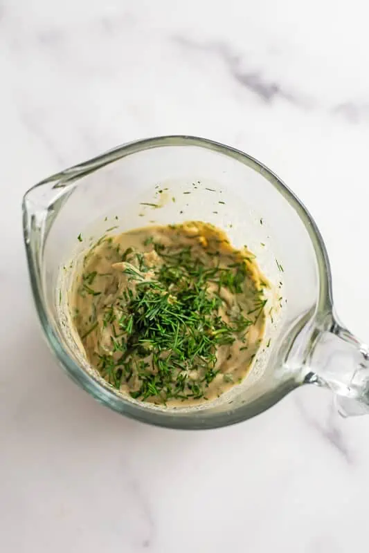 Creamy vegan dill dressing ingredients combined in a measuring cup.