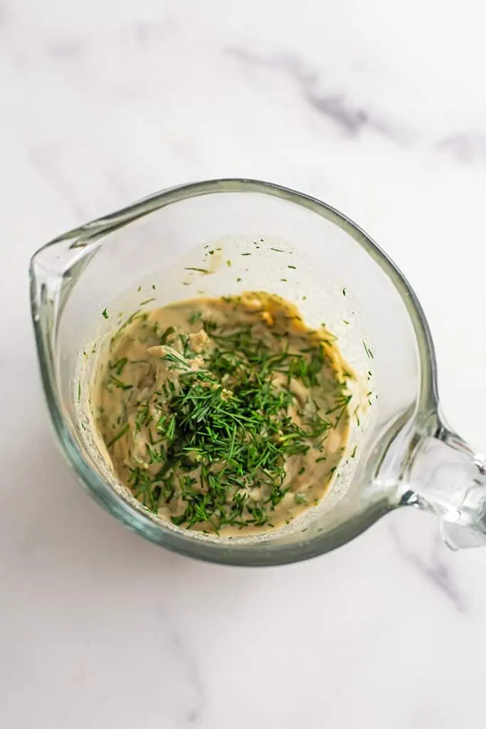 Creamy vegan dill dressing ingredients combined in a measuring cup.