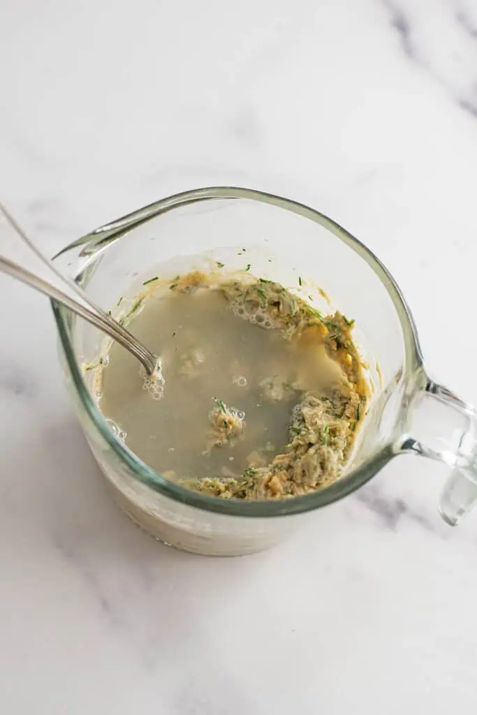 Creamy vegan dill dressing ingredients with water in measuring cup.