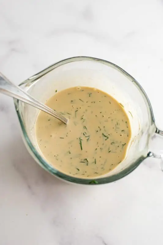 Creamy vegan dill dressing fully combined in a measuring cup.